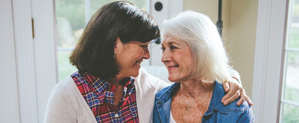 Woman and her elderly mom facing each other smiling.